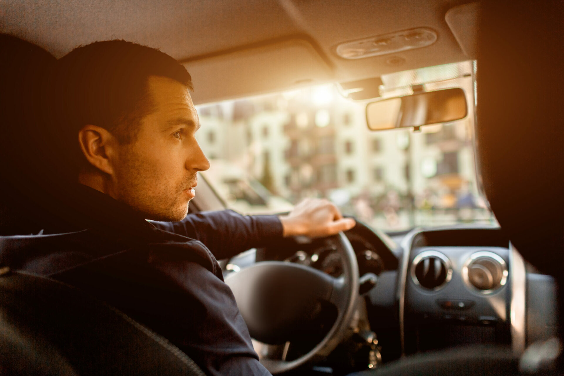 A man sits in a car cabin in and looks out at the street. Taxi driver in his car. Transportation concept