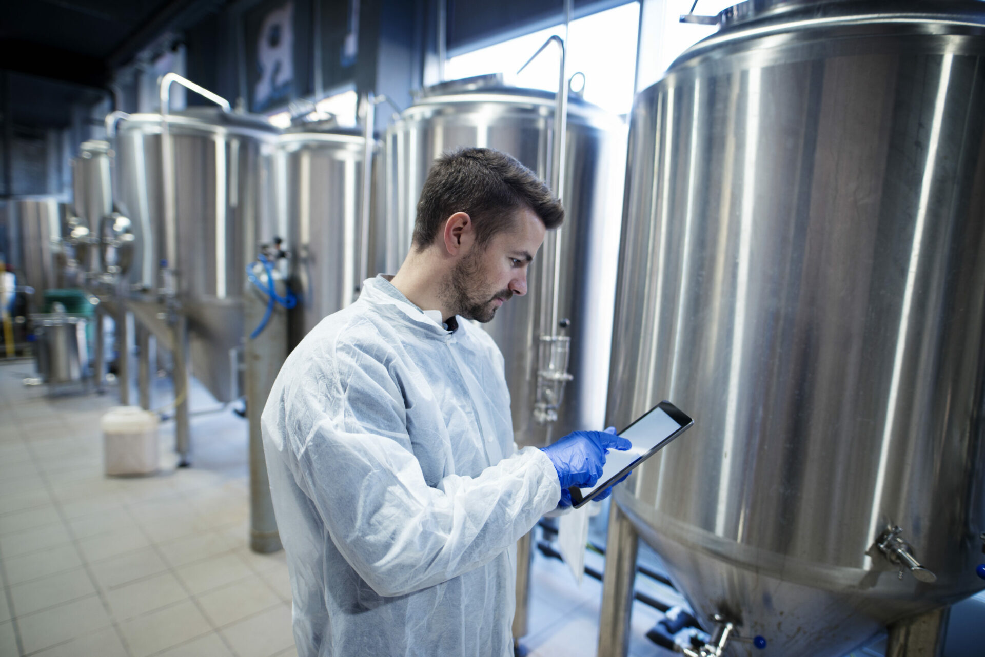 Technologist expert standing in food production plant and typing on his tablet computer.
