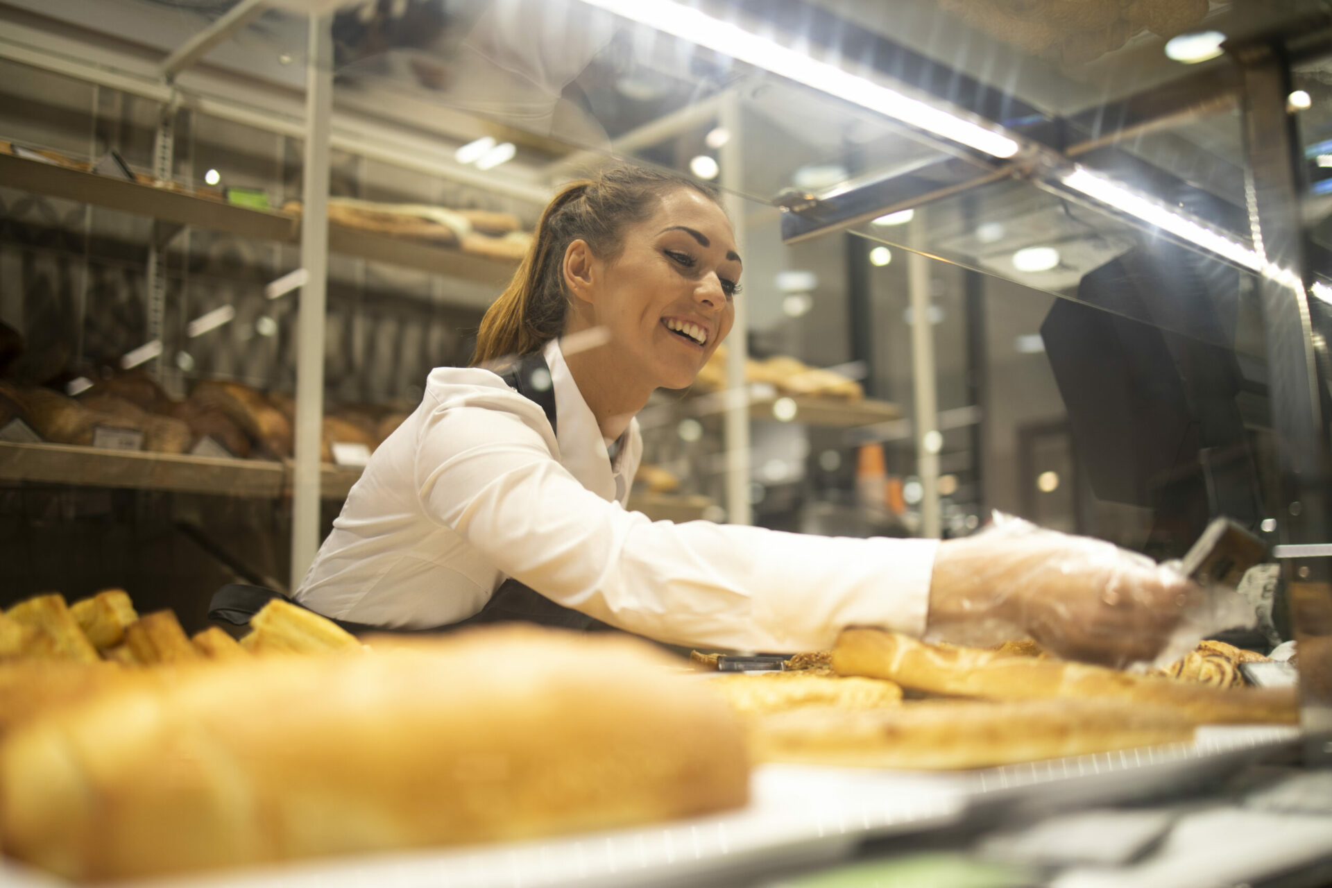 Woman preparing bread for sale in supermarket bakery department.