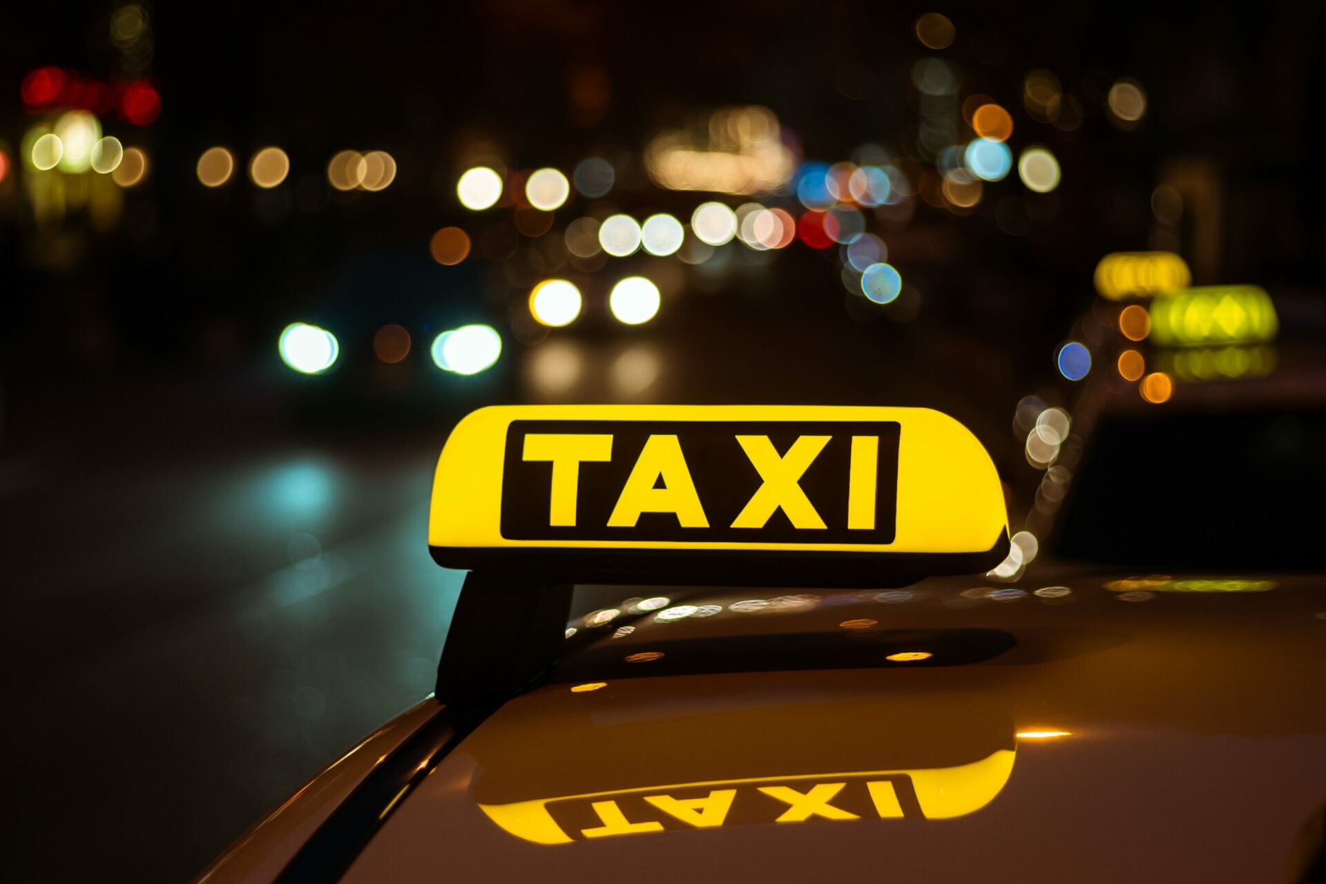 A yellow and black sign of Taxi placed on top of a car at night